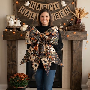 Op de afbeelding: Een grote decoratieve strik met een patchworkpatroon van Halloween-illustraties, waaronder zwarte katten, oranje pompoenen, spinnenwebben, geesten en heksenhoeden op een donkere achtergrond met puntige uiteinden.