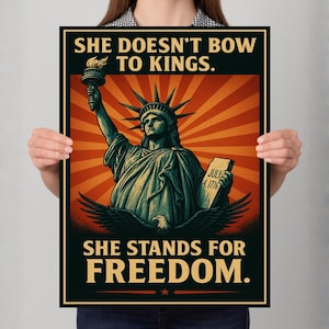 May include: A poster featuring the Statue of Liberty with the text "SHE DOESN'T BOW TO KINGS. SHE STANDS FOR FREEDOM." The artwork has a vintage style with a red and orange sunburst background and a black border.