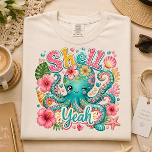 May include: Cream-colored t-shirt featuring a teal octopus with floral accents and the words "Shell Yeah." The design includes pink hibiscus flowers, seashells, and hearts. The shirt is part of the Coastal Dreams Collection.