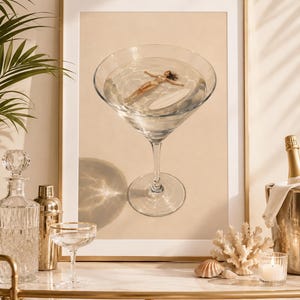 May include: A framed wall art print featuring a large martini glass filled with clear liquid. Inside the glass, a person in a white bikini floats on their back next to a white surfboard. The background of the print is a solid light beige color.