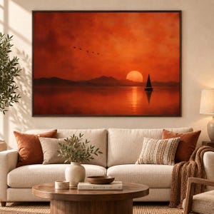 Pode incluir: Uma impressão de arte de parede retangular apresentando um pôr do sol laranja vibrante sobre um corpo de água calmo. Um pequeno veleiro está silhuetado no lado direito, com montanhas distantes ao fundo e um pequeno bando de pássaros no céu.