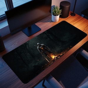 Könnte beinhalten: Schwarze rechteckige Schreibtischunterlage mit einer digitalen Illustration eines Ritters in Rüstung, der in der Nähe eines Feuers in einem dunklen Wald steht. Der Ritter hält ein Schwert. Die Matte liegt auf einem Holzschreibtisch mit einem Computermonitor und einer Topfpflanze.