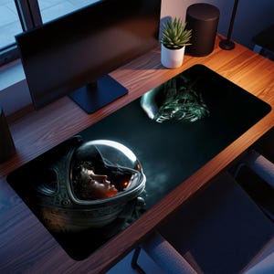 Puede incluir: Alfombrilla de escritorio rectangular negra con una escena de ciencia ficción. Representa a un astronauta con un traje espacial frente a una criatura alienígena amenazante. La cara del astronauta es visible dentro del casco. El fondo es oscuro con un efecto de humo.