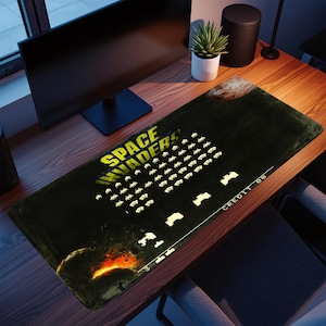 May include: Black rectangular desk mat featuring the Space Invaders arcade game. The mat has a yellow and white graphic of the game's logo and alien invaders. The words "CREDIT 00" are printed on the mat.