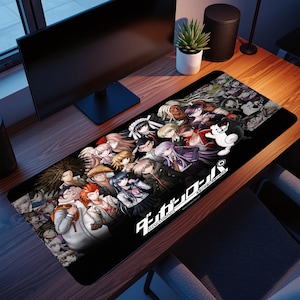 May include: A black rectangular mousepad with a vibrant anime-style design featuring numerous characters. The mousepad displays the Japanese text "Danganronpa" in white. The design includes various character portraits and a white cartoon bear.