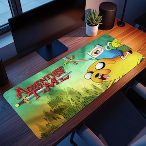 May include: A rectangular Adventure Time mousepad featuring Finn and Jake. The mousepad has a green and yellow background with the Adventure Time logo and a sword. The mousepad is on a wooden desk.