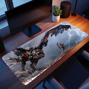 May include: A rectangular mousepad featuring a detailed illustration of a mechanical creature and a character with a bow and arrow, set against a stormy sky. The mousepad has the text "Horizon Zero Dawn" at the bottom.