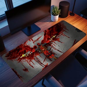 May include: A rectangular desk mat featuring a graphic of the Deadpool character in a red and black suit, with red wing-like patterns and holding two guns. The background is gray with red splatter effects.