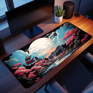May include: A rectangular desk mat with a Japanese landscape design. The artwork shows a large full moon, a pagoda, and pink cherry blossom trees against a blue sky and clouds. The mat is on a wooden desk.