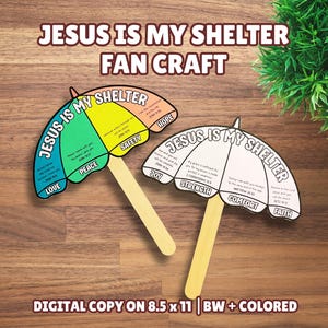 May include: Two umbrella-shaped paper crafts with wooden sticks. One is colored in blue, green, yellow, and peach with the text 'JESUS IS MY SHELTER', 'LOVE', 'PEACE', 'SAFETY', and 'HOPE'. The other is black and white with 'JOY', 'STRENGTH', 'COMFORT', and 'FAITH'.