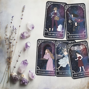 May include: A collection of tarot cards featuring illustrations of women with titles like "The Girl Boss" and "The Superwoman." The cards have a starry background and are framed with a decorative border. Amethyst crystals and lavender sprigs are arranged around the cards.