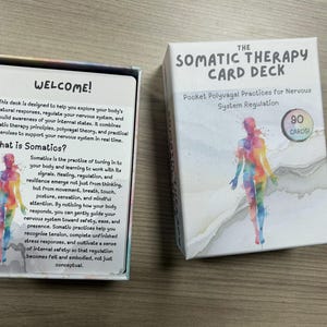 Może przedstawiać: Białe pudełko i otwarta talia kart zatytułowana The Somatic Therapy Card Deck. Pudełko zawiera akwarelową sylwetkę człowieka i napis 90 CARDS. Otwarta karta zawiera tekst Welcome! oraz What is Somatics? wraz z akwarelową sylwetką.