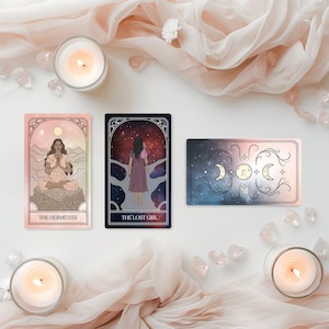 May include: Three tarot cards with illustrations and text, including "THE HERMITESS" and "THE LOST GIRL", are arranged with lit candles, crystals, and draped fabric. The cards feature celestial and feminine imagery in soft colors.