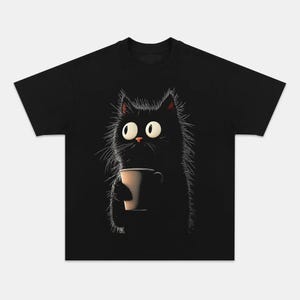 May include: Black t-shirt featuring a cartoon cat with large eyes, holding a coffee cup. The cat has fluffy fur and a surprised expression. The design is simple and whimsical, perfect for cat lovers.