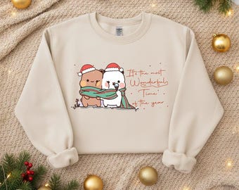 May include: Beige sweatshirt featuring a cartoon illustration of two bears wearing Santa hats and a green scarf. The text "It's the most Wonderful Time of the year" is written in red script. Christmas-themed apparel.