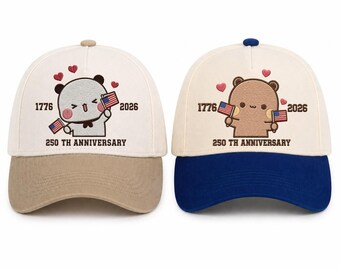 May include: Two baseball caps with embroidered designs. One has a tan bill and a gray bear holding an American flag, the other has a blue bill and a brown bear. Both caps have the text "1776 2026 250TH ANNIVERSARY".