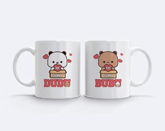 May include: Two white ceramic mugs with matching designs. One mug features a panda bear holding a heart with the text "HE IS MY DUDU". The other mug has a brown bear holding a heart with the text "SHE IS MY BUBU".