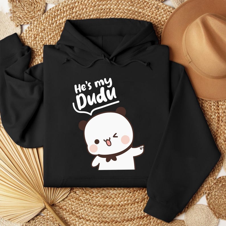 May include: Black hoodie featuring a white panda illustration with a bow tie, winking and pointing. The text "He's my Dudu" is above the panda. The hoodie has a drawstring hood and long sleeves.