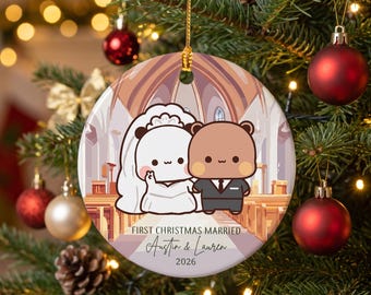 May include: A round ceramic Christmas ornament featuring a cartoon illustration of a bear couple in wedding attire inside a church. The text reads FIRST CHRISTMAS MARRIED, Austin & Lauren, and 2026. It hangs from a gold string on a pine tree.