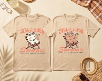 May include: Two beige t-shirts with matching graphics. Each shirt features a cartoon animal in sunglasses relaxing in a beach chair with a drink. The text "SILLY BUBU" and "SILLY DUDU" are above the word "Summer". The phrase "JUST A SILLY BUBU GETTIN LOOSE" is below.