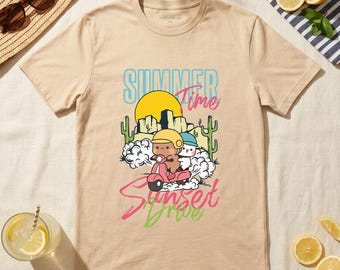 May include: Beige t-shirt with a graphic of two cartoon characters riding a pink scooter in front of a desert sunset. The text "Summer Time Sunset Drive" is above and below the image in blue, pink, and green.