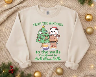 May include: Beige sweatshirt with a Christmas-themed graphic. The graphic features a decorated Christmas tree and two cartoon characters. Text on the sweatshirt reads "From the windows to the walls I'm about to deck these halls."