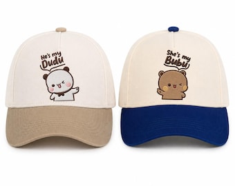 May include: Two baseball caps with cartoon bear graphics. One cap is beige and brown with the text "He's my Dudu". The other cap is beige and blue with the text "She's my Bubu". Both caps have a curved brim.
