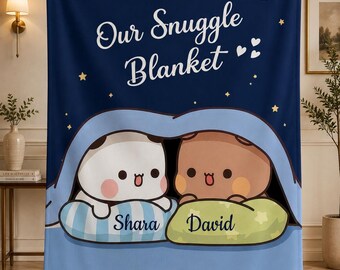 May include: A navy blue fleece blanket featuring the text Our Snuggle Blanket, a yellow crescent moon, and stars. Below, two cartoon characters, one white and one brown, rest on pillows labeled Shara and David under a light blue blanket.