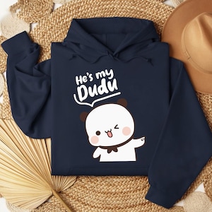 May include: Navy blue hoodie featuring a cartoon panda with a wink and the text "He's my Dudu" in white. The panda has a black bow tie and brown ears. The hoodie is made of a soft material.