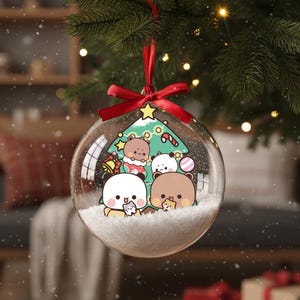 May include: Clear Christmas ornament with a red ribbon and bow, hanging from a green tree branch. Inside the ornament are cartoon bears and a Christmas tree design, with white snow at the bottom. The ornament is round.