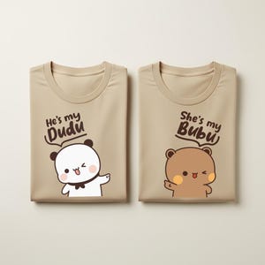 Peut inclure: Deux t-shirts beiges avec des motifs assortis d'ours et de pandas de dessins animés. L'un dit "He's my Dudu" avec un panda blanc, l'autre "She's my Bubu" avec un ours brun. Col rond.