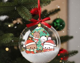 May include: A clear glass Christmas ornament with a red ribbon, hanging on a Christmas tree. Inside the ornament is a winter scene with cartoon bears and pandas wearing Santa hats and scarves, with a Christmas tree.