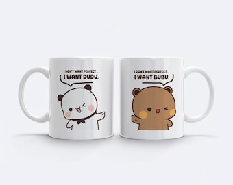 May include: Two white ceramic mugs with black text and cartoon bear illustrations. One mug features a panda bear and the text "I WANT DUDU." The other mug has a brown bear and the text "I WANT BUBU."
