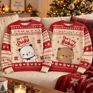 Pode incluir: Dois suéteres de malha creme e vermelhos com padrões festivos. O suéter da esquerda exibe um panda branco com o texto He's my Dudu. O da direita apresenta um urso marrom com o texto She's my Bubu. Ambos têm mangas compridas e gola redonda.
