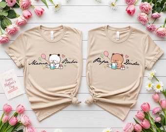 May include: Two beige t-shirts with matching cartoon bear graphics. One shirt says "Mama Bubu" and the other says "Papa Dudu". The shirts are surrounded by pink roses, daisies, and a "Happy Mother's Day" card.