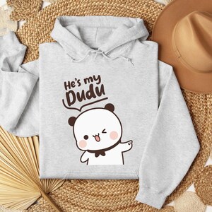 May include: A light gray hoodie with the text "He's my Dudu" above a cartoon panda bear. The panda has black ears, a black bow tie, and is winking. The hoodie has a drawstring hood and long sleeves.
