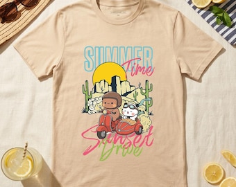 May include: Beige t-shirt with a colorful graphic of two cartoon characters on a red scooter with a sidecar, set against a desert landscape and a yellow sun. The text "Summer Time Sunset Drive" is displayed above and below the image.