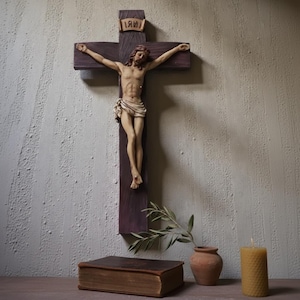 Puede incluir: Un crucifijo de madera con una figura esculpida de Jesucristo. La cruz es de color marrón oscuro con una figura marrón más clara. La figura tiene pelo largo y un taparrabos. Una pequeña pancarta sobre la figura dice "INRI". Un libro, una vela y un jarrón están en primer plano.