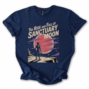 May include: Navy blue t-shirt with a retro sci-fi graphic. The design shows a figure on a cliff, a red planet, and the text "The Rise and Fall of Sanctuary Moon". The sleeves are rolled up.