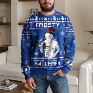May include: A blue long-sleeve sweatshirt featuring a repeating white snowflake and dumbbell pattern. The centre graphic depicts a muscular snowman wearing a black top hat and lifting a dumbbell, with the text FROSTY THE SWOLEMAN printed.