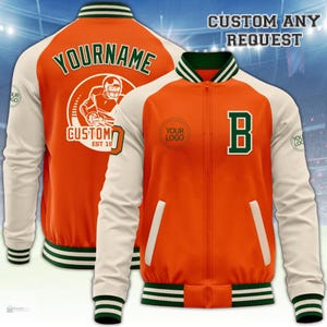 Puede incluir: Una chaqueta universitaria en naranja y blanco roto con ribetes acanalados a rayas verdes. La espalda muestra el texto YOURNAME y CUSTOM con un gráfico de jugador de fútbol americano. El frente tiene una B verde, un círculo YOUR LOGO y dos bolsillos.