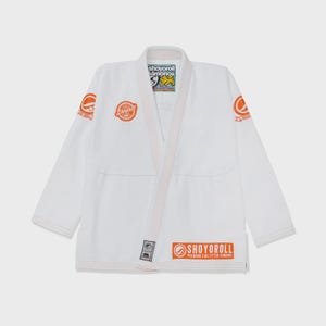 Op de afbeelding: Witte vechtsportuniform met oranje accenten. Het uniform toont de tekst "SHOYOROLL" in oranje op de borst, mouwen en onderkant. Ontworpen voor vechtsporttraining en -competitie.