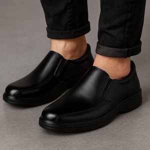 Pu&ograve; includere: Un paio di scarpe nere in pelle senza lacci. Le scarpe hanno una punta arrotondata e una suola bassa e spessa. La tomaia &egrave; liscia e lucida, con un piccolo pannello elastico sul lato. Le scarpe sono indossate con pantaloni neri.