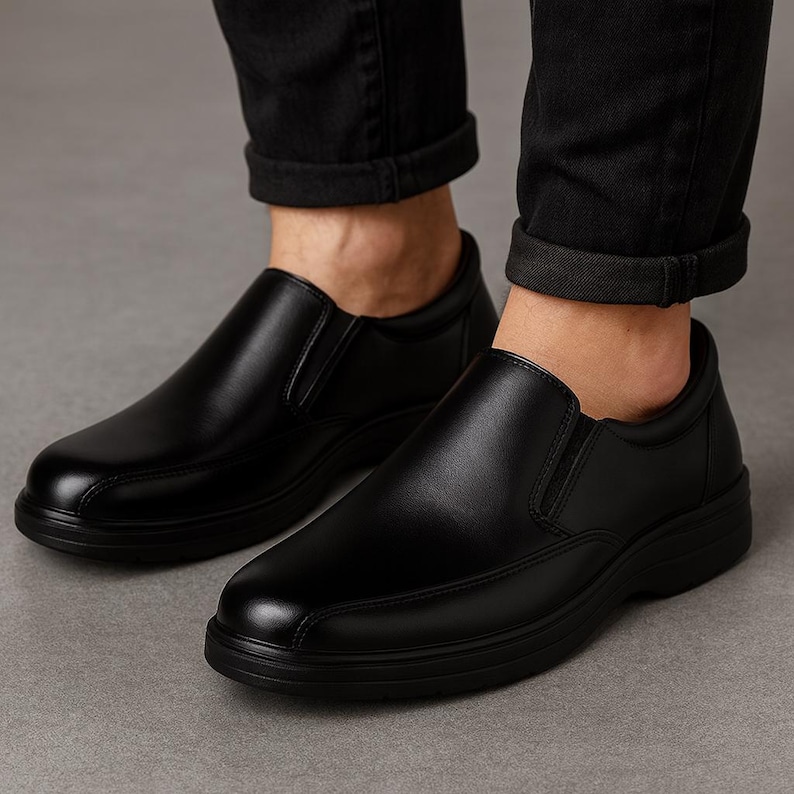 Pu&ograve; includere: Un paio di scarpe nere in pelle senza lacci. Le scarpe hanno una punta arrotondata e una suola bassa e spessa. La tomaia &egrave; liscia e lucida, con un piccolo pannello elastico sul lato. Le scarpe sono indossate con pantaloni neri.
