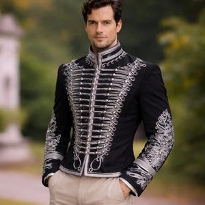 Può includere: Giacca nera in stile militare con abbellimenti argentati. La giacca presenta un colletto alto, finiture argentate decorative e più file di trecce argentate sul petto. Le maniche sono decorate con ricami argentati intricati. I pantaloni sono beige.
