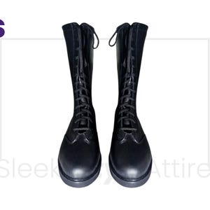 Puede incluir: Un par de botas negras hasta la rodilla con dise&ntilde;o de cordones. Las botas tienen punta redondeada y tac&oacute;n bajo. Las botas est&aacute;n hechas de un material liso similar al cuero. Las botas se muestran sobre un fondo blanco.