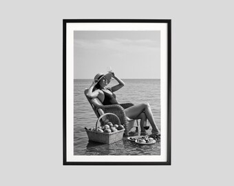 May include: Black and white framed print of a person relaxing in a wicker chair in the ocean. A straw hat and a glass of wine are held up. A basket of fruit and a plate of food are nearby.