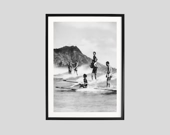 May include: Monochrome framed print showing people surfing. The image features several figures riding waves, with a mountain visible in the background. The print is enclosed in a black frame.