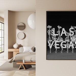May include: Black and white framed print featuring the text "LAS VEGAS" with showgirls. The image shows the showgirls holding up the letters. The print is displayed on a beige wall.