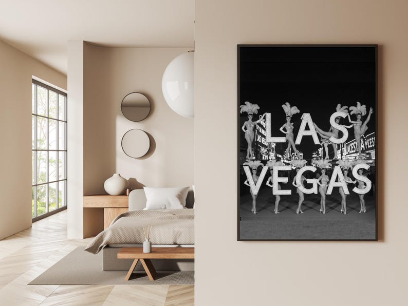 May include: Black and white framed print featuring the text "LAS VEGAS" with showgirls. The image shows the showgirls holding up the letters. The print is displayed on a beige wall.